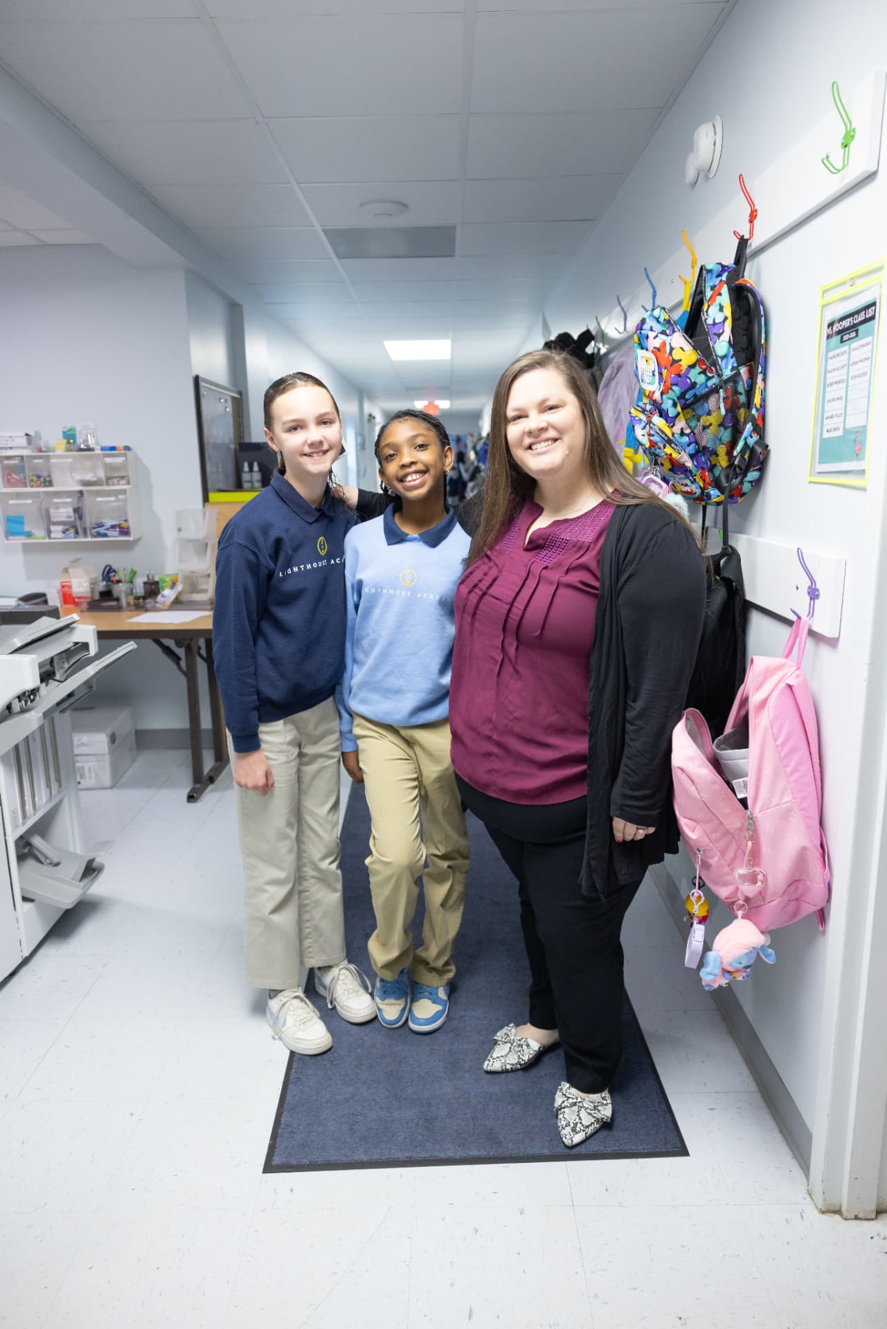 Two students smiling with their teacher in a Lighthouse Academy hallway