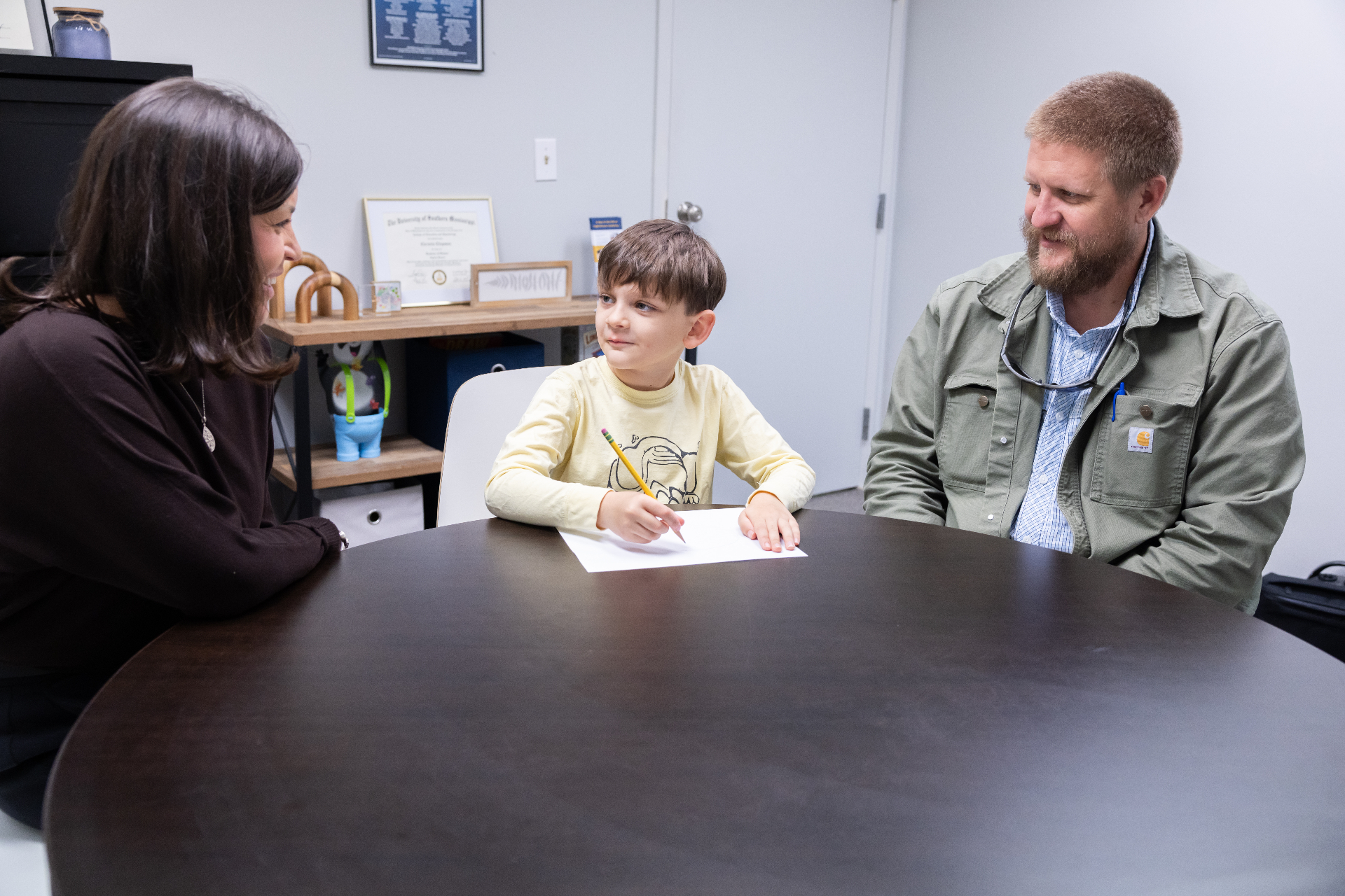 Child working at table with parent and evaluator